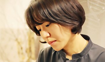 조윤주 원장 — 짙은 회색 진료복, 아래를 보는 옆모습(따뜻한 실내 조명)